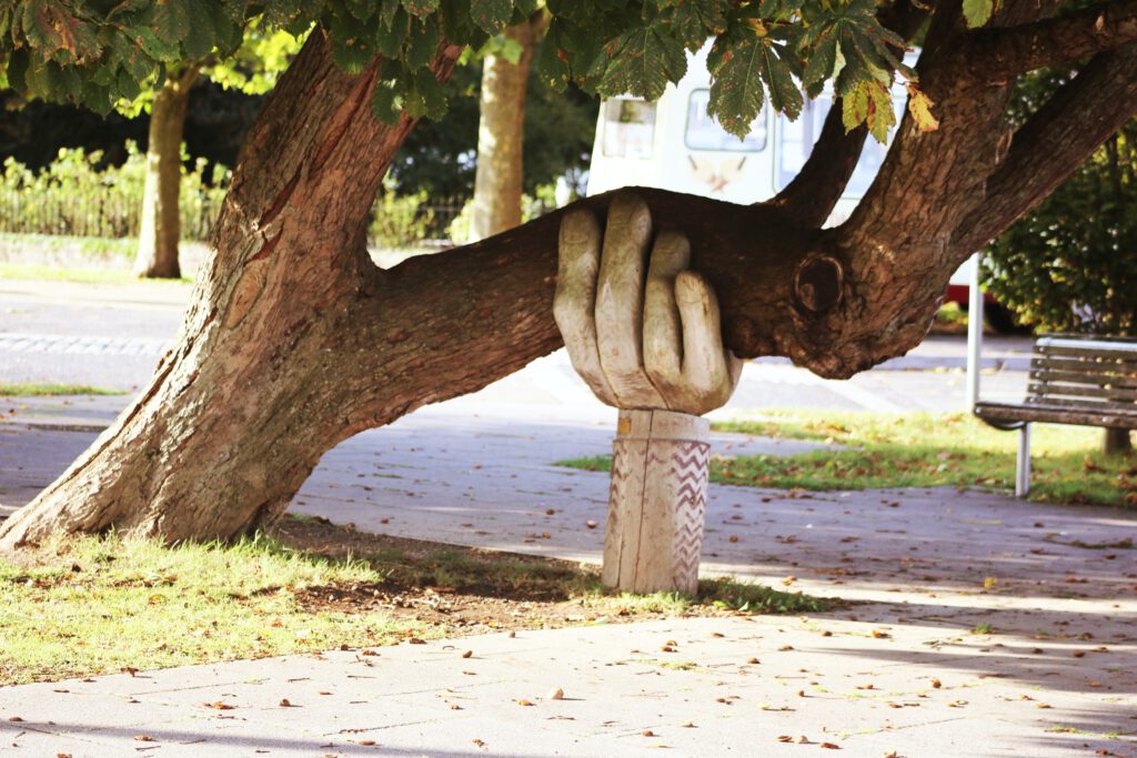 Carved hand standing on the earth supporting a large tree branch growing  sideways from large tree